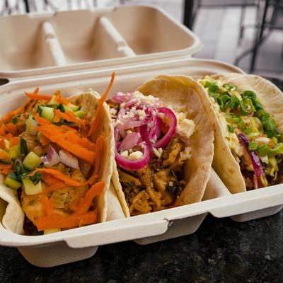 Three tacos with different toppings in a takeout container.