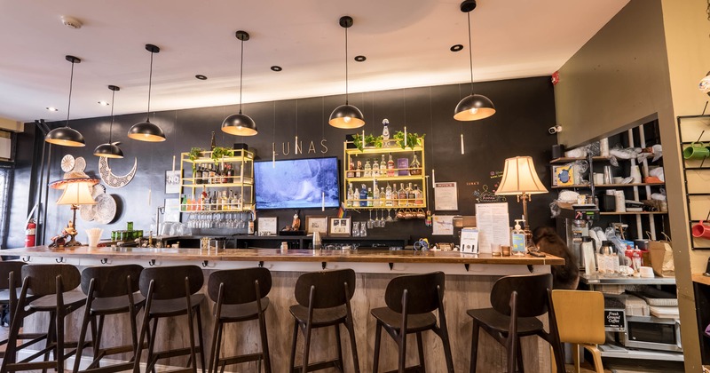 Interior of a modern bar with wooden stools, pendant lights, and shelves with bottles
