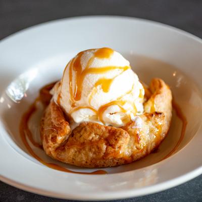 Apple tart topped with a scoop of ice cream and a drizzle of caramel sauce.