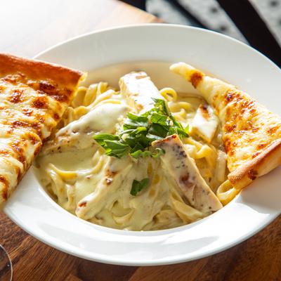 Chicken Alfredo pasta served with cheesy bread on the side.