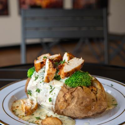 Baked potato with grilled chicken, Alfredo sauce, and broccoli.