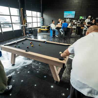 Person playing pool with others socializing in the background.