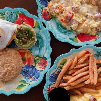 An overhead view of colorful plates featuring scrambled eggs, fries, and guacamole on a bun.