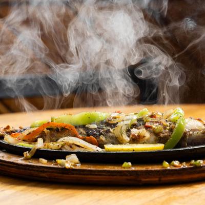 Sizzling grilled red snapper with vegetables and steam rising from the dish.