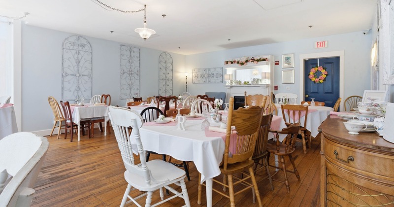 A vintage dining room with mixed wooden chairs, tables with white cloths