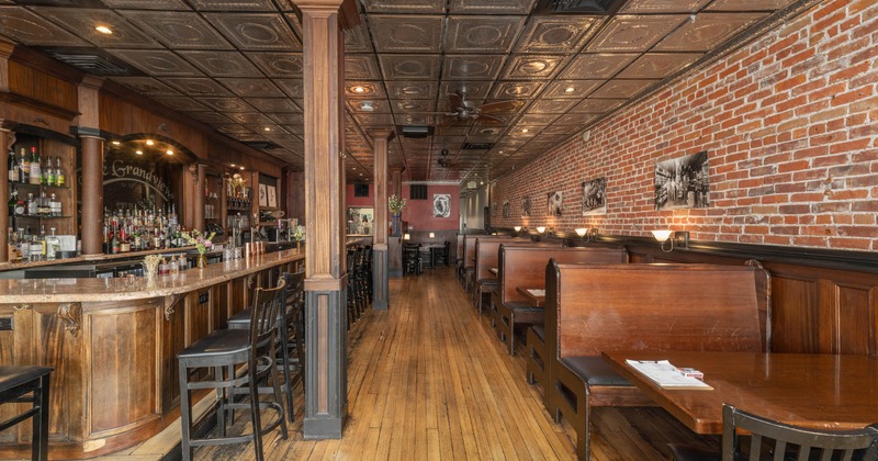 Interior, bar with stools on the left, wooden seating booths on the right, hardwood flooring
