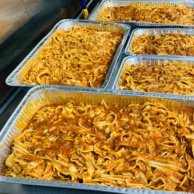Five large foil pans filled with tagliatelle with meat sauce.