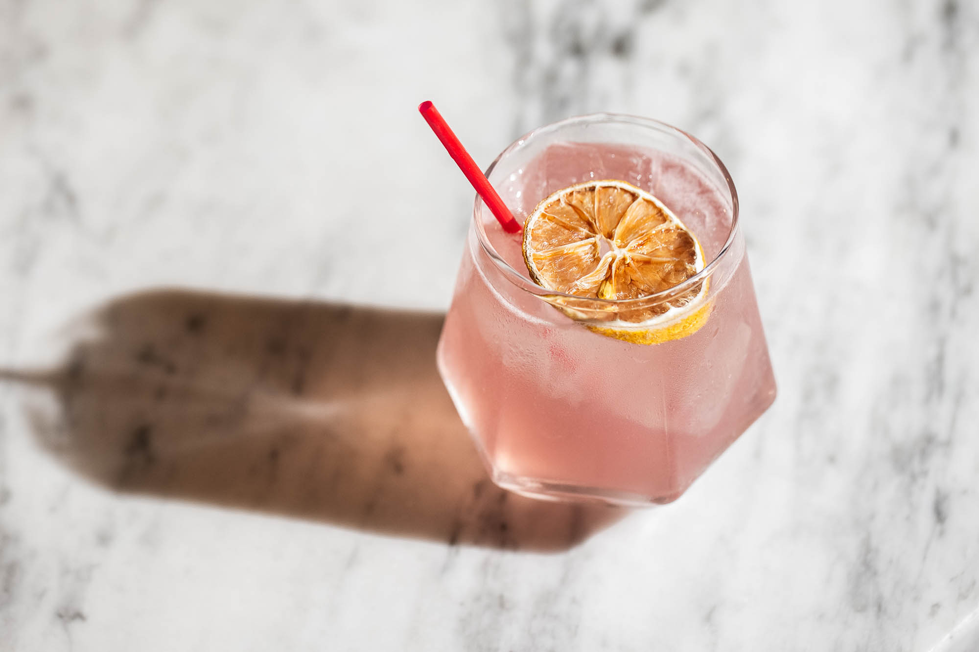 A pink colored Summer Madness cocktail, garnished with a dehydrated lemon wheel