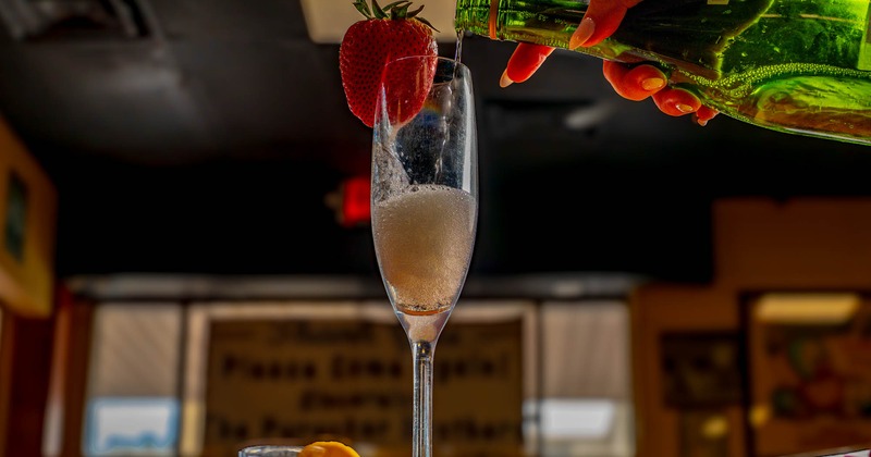 Interior, sparkling wine being poured into a flute adorned with a fresh strawberry