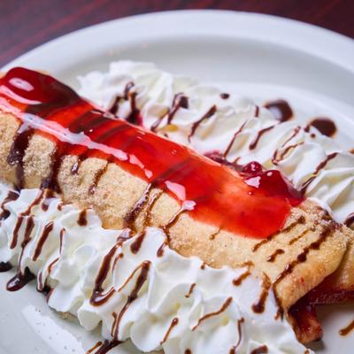 Cheesecake burrito with whipped cream, strawberry sauce, and chocolate drizzle.