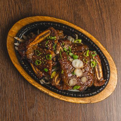BBQ Short Rib served on a sizzling hot cast-iron platter placed over a wooden board.