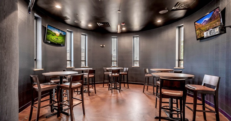 Interior, round space with round tables and bar chairs, and TVs on the wall