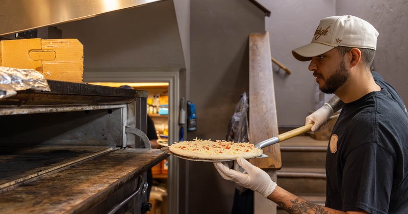 A pizza maker about to place pizza dough with topping into an oven