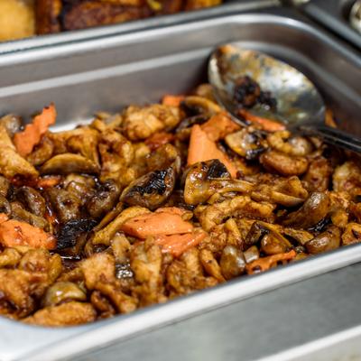A metal buffet tray filled with stir-fried chicken, mushrooms, and carrots.