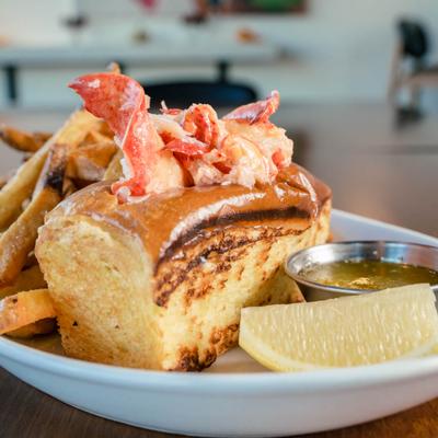 Lobster roll with fries, dip and lemon wedge on the side.