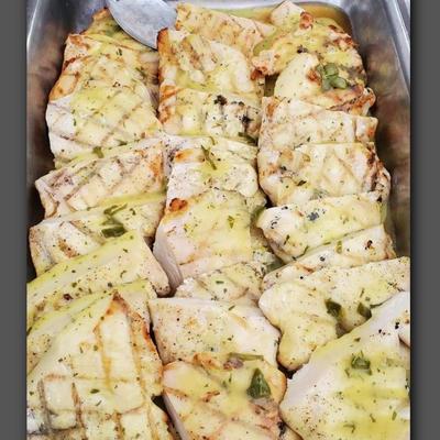 Grilled chicken breasts with a light herb sauce, arranged in metal tray.