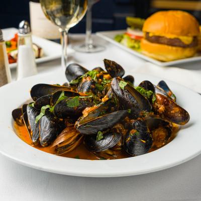 Mussels served in tomato broth, beside a glass of white wine.