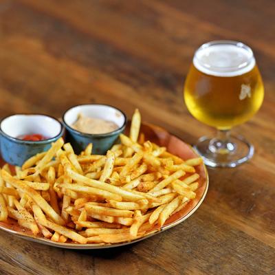 A plate of fries with dipping sauces and a glass of beer.