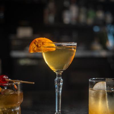Golden cocktail in a stemmed glass with an orange slice garnish.