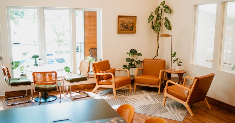 Bright living room with mid-century modern furniture, leather chairs, green plants, and large windows