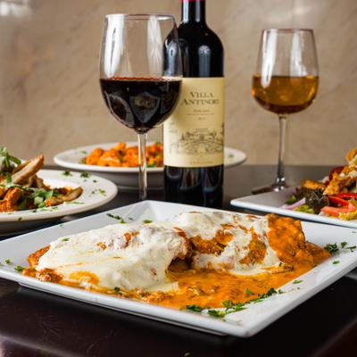 Chicken alla vodka with wine glasses and food plates behind.