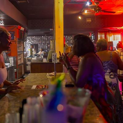 People socialize at a dimly lit bar, a customer is  talking to an employee.