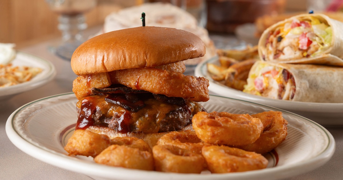 Burger topped with onion rings beside fried potato rounds