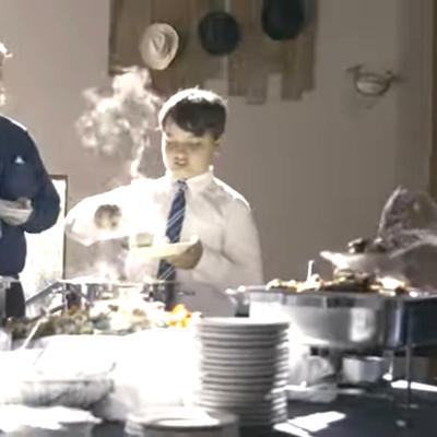 Child serving food at a buffet table with steaming dishes.