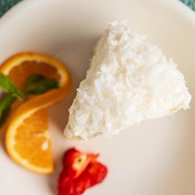 Coconut Cake served on a white ceramic plate with orange slice and strawberry garnish.
