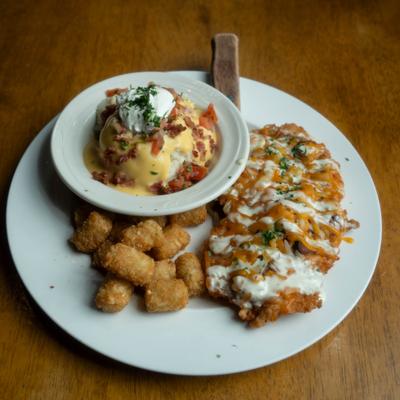 Buffalo chicken cutlet served with tater tots and a bowl of rice with sauce and bacon bits.