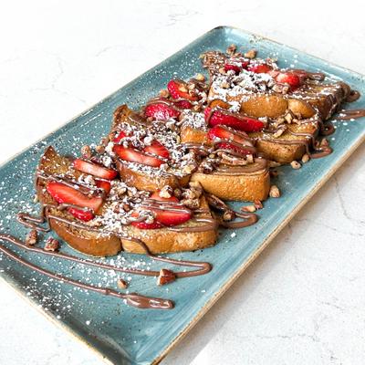 French toast topped with powdered sugar, nuts, strawberries and chocolate sauce.