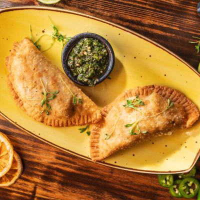 Two beef empanadas served with chimichurri sauce on a yellow plate.
