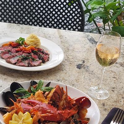 A seafood platter served on an outdoor table with a sliced steak dish and wine.