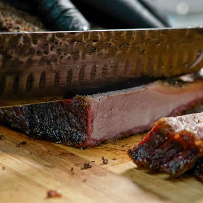 Smoked brisket being sliced with a large knife on a wooden board.