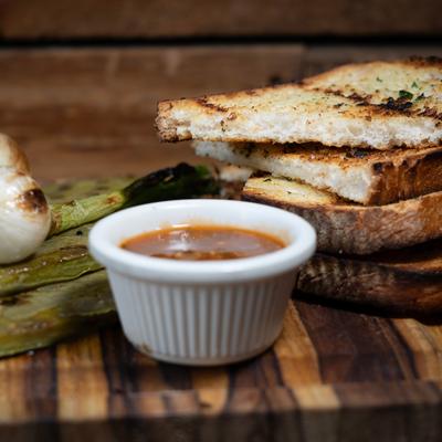 Grilled bread slices with dipping sauce, garlic, and grilled green onions.