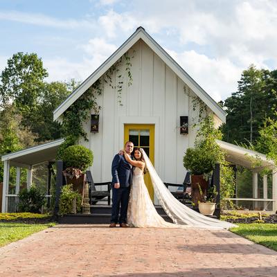A wedding couple stands joyfully in front of a white building with a yellow door