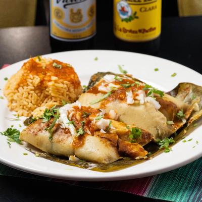 Tamales wrapped in banana leaves served with salsa, crema, cilantro, and Mexican rice.