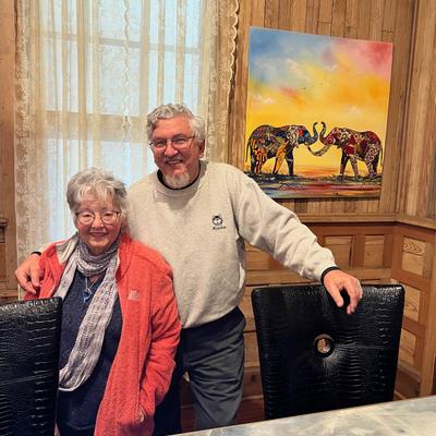Two people by a table with a colorful elephant painting on the wall behind them.