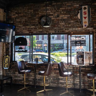Interior, high seating area by the window, tables with stools, brick walls, TV on the wall.