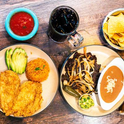 Breaded chicken and carne asada plates with rice, avocado, beans, and salsa.