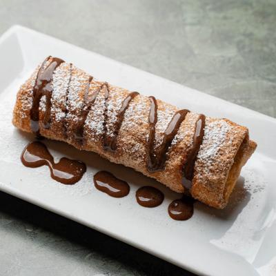 Fried cheesecake chimichanga topped with powdered sugar and chocolate drizzle.