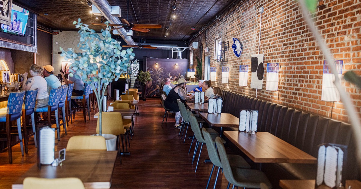 Interior of a modern restaurant with a bar and brick wall, wooden tables and chairs