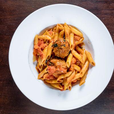 Penne pasta in a tomato sauce topped with two meatballs.