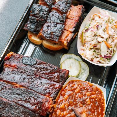 A plate with Four Bones St. Louis Ribs and Burnt ends served with coleslaw and BBQ beans.