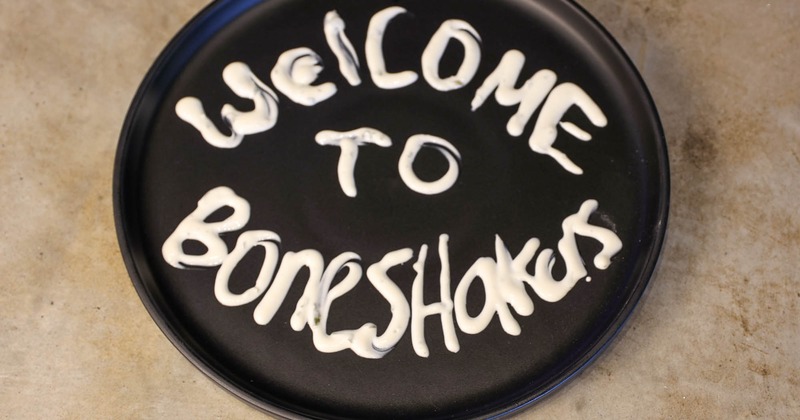 Black round plate with Welcome to Boneshakers written in a white creamy sauce
