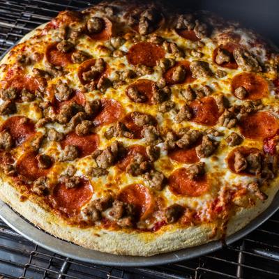 Pizza topped with cheese, pepperoni slices and crumbled Italian sausage.