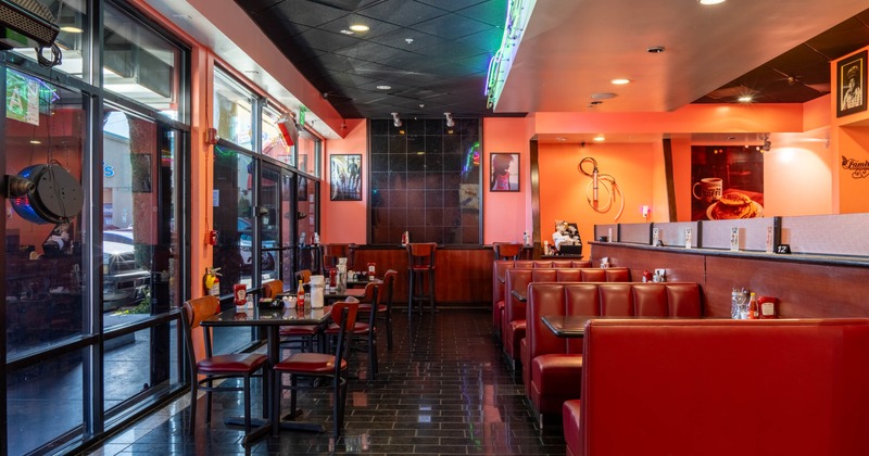 Interior of a retro-style diner with red booths, black tiled floor and large windows.
