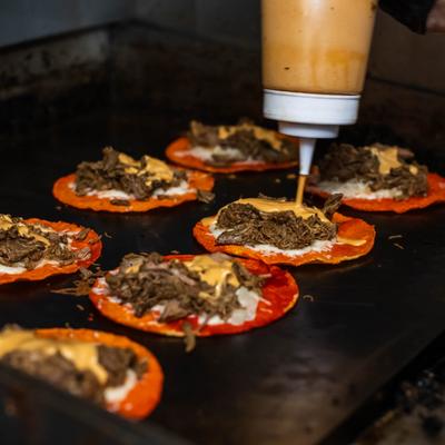 Open-faced tacos being topped with sauce.