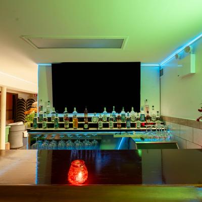 The interior of a modern fully stocked bar with LED strip lighting and a large screen.