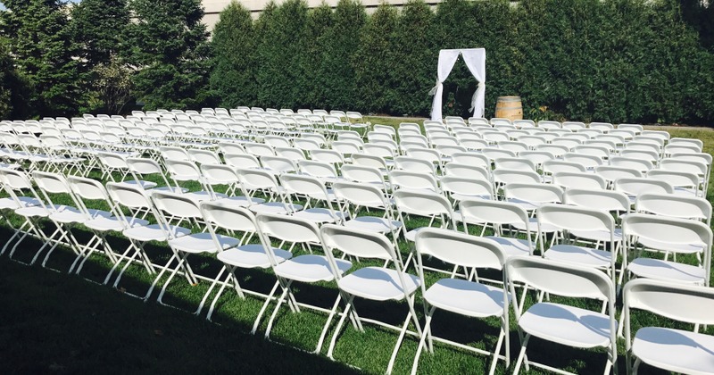 Outdoor on site wedding ceremony with rows of white chairs on the green grass.